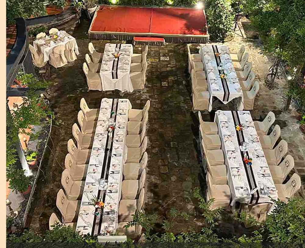 Long banquet tables dressed in white linen and set for dinner in the hotel's garden courtyard, seen from above