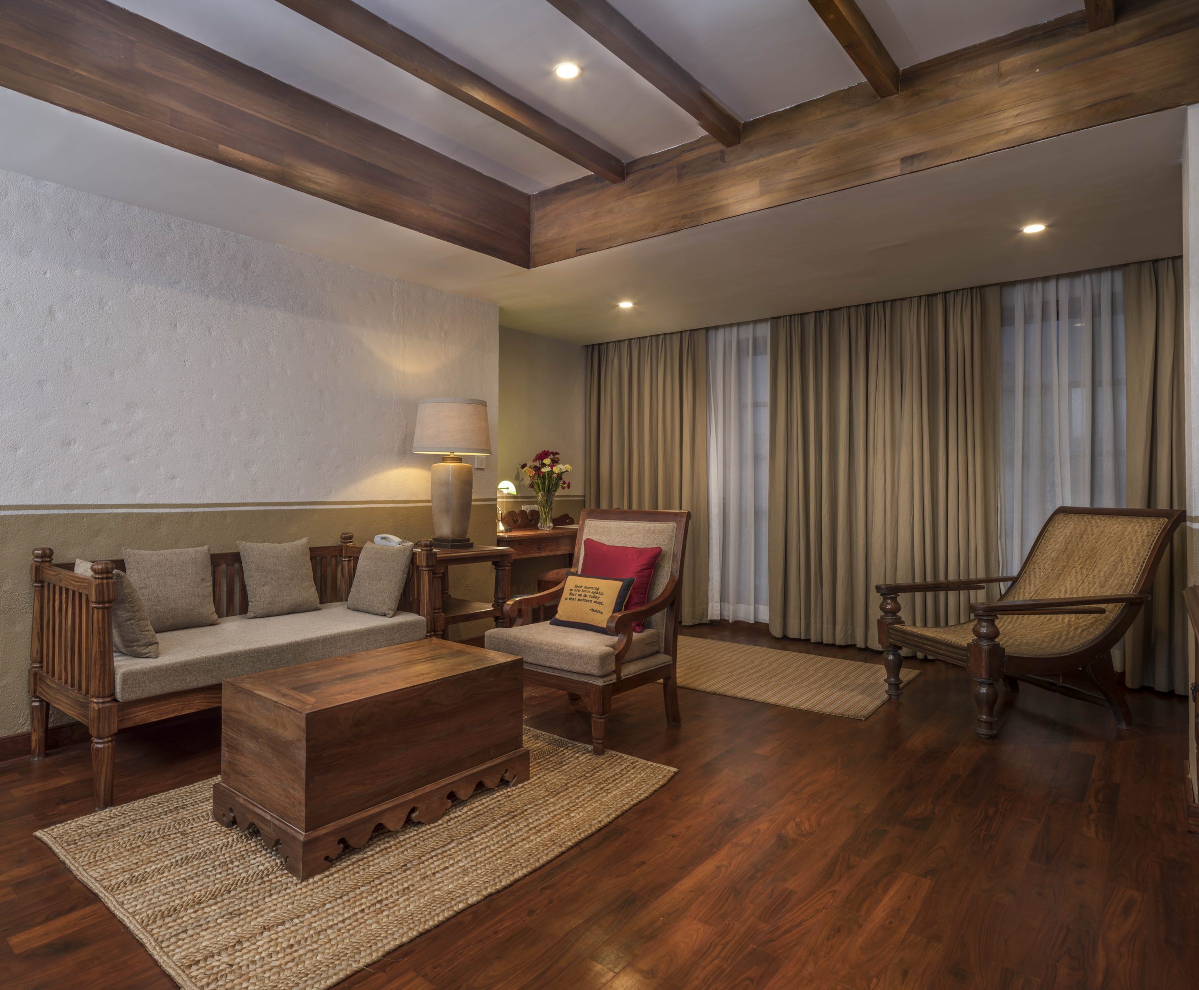 The separate living room of the Executive Suite, with a timber-beamed ceiling, daybed, and a caned planter&rsquo;s chair by the window