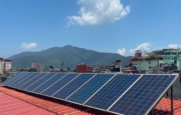 Rooftop solar panels at Nepali Ghar against the Kathmandu skyline and hills