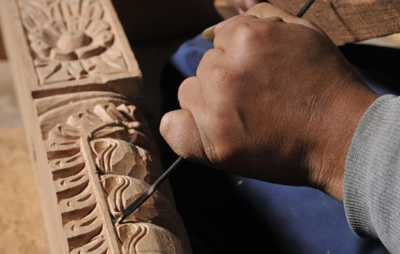 A craftsman&rsquo;s hands chiselling a floral frieze into a timber beam at a Newari wood-carving workshop